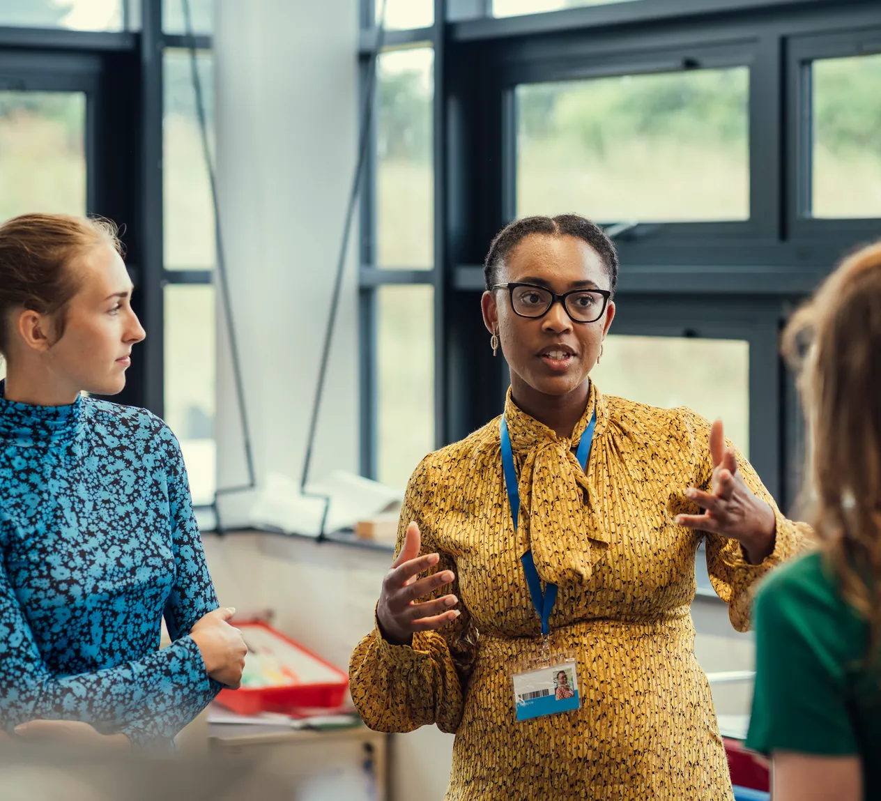 A teacher in a yellow dress talking with a group of sixth-form students in a classroom