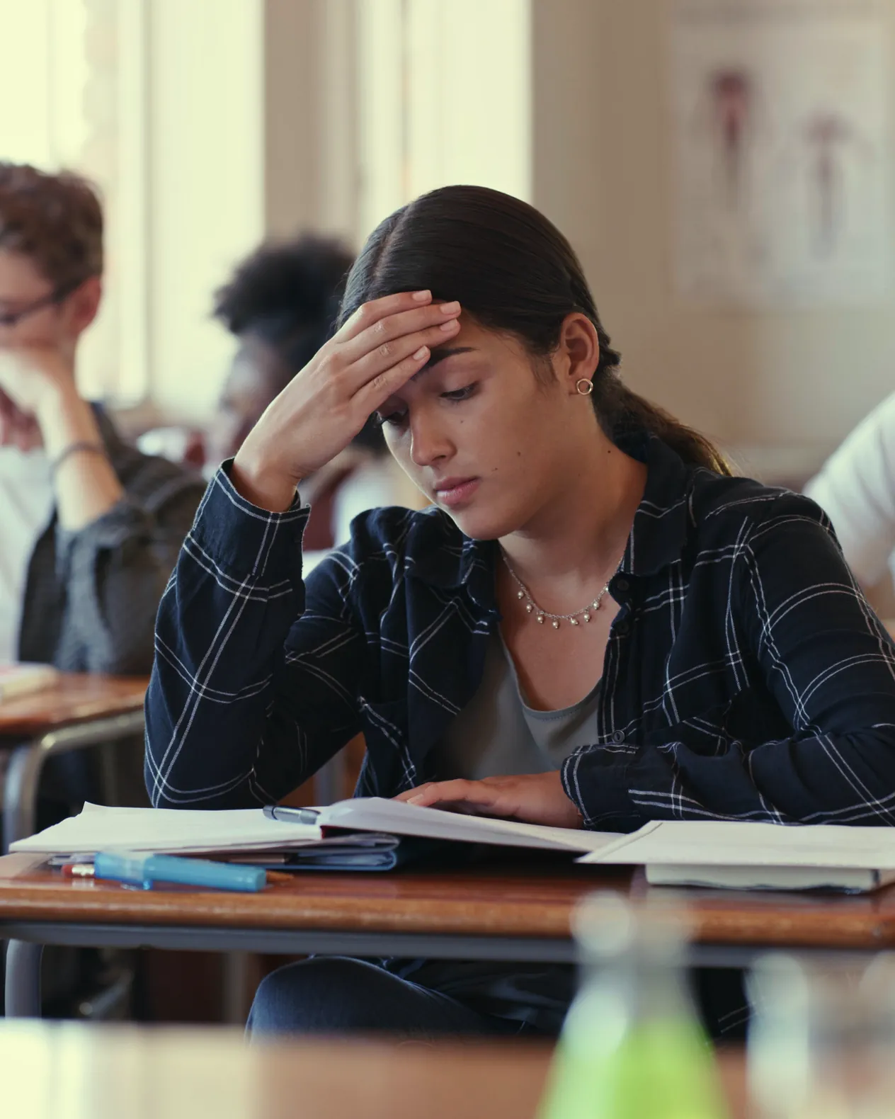 A student at her desk with a hand to her forehead, frowning over an open textbook